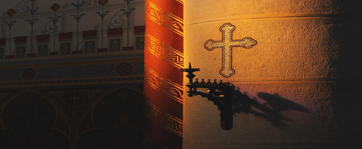 Golden cross illuminated by warm light on a church wall with ornate architectural details.
