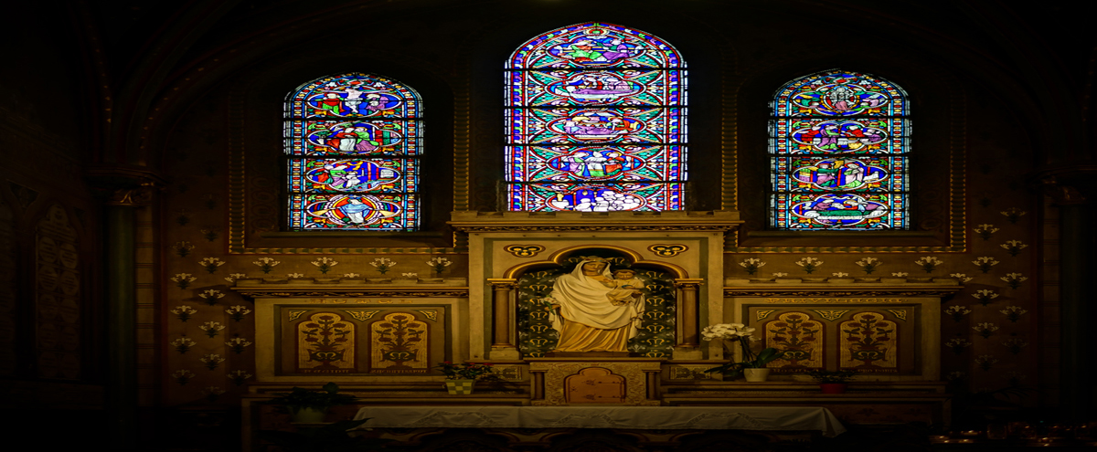 Church altar with a statue of the Virgin Mary and child, illuminated by colorful stained-glass windows